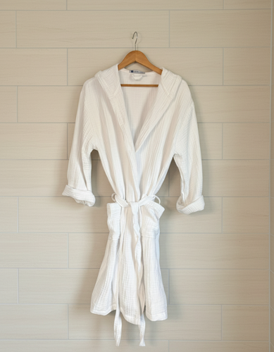 White muslin cotton robe  with a belt on a hanger against a white background